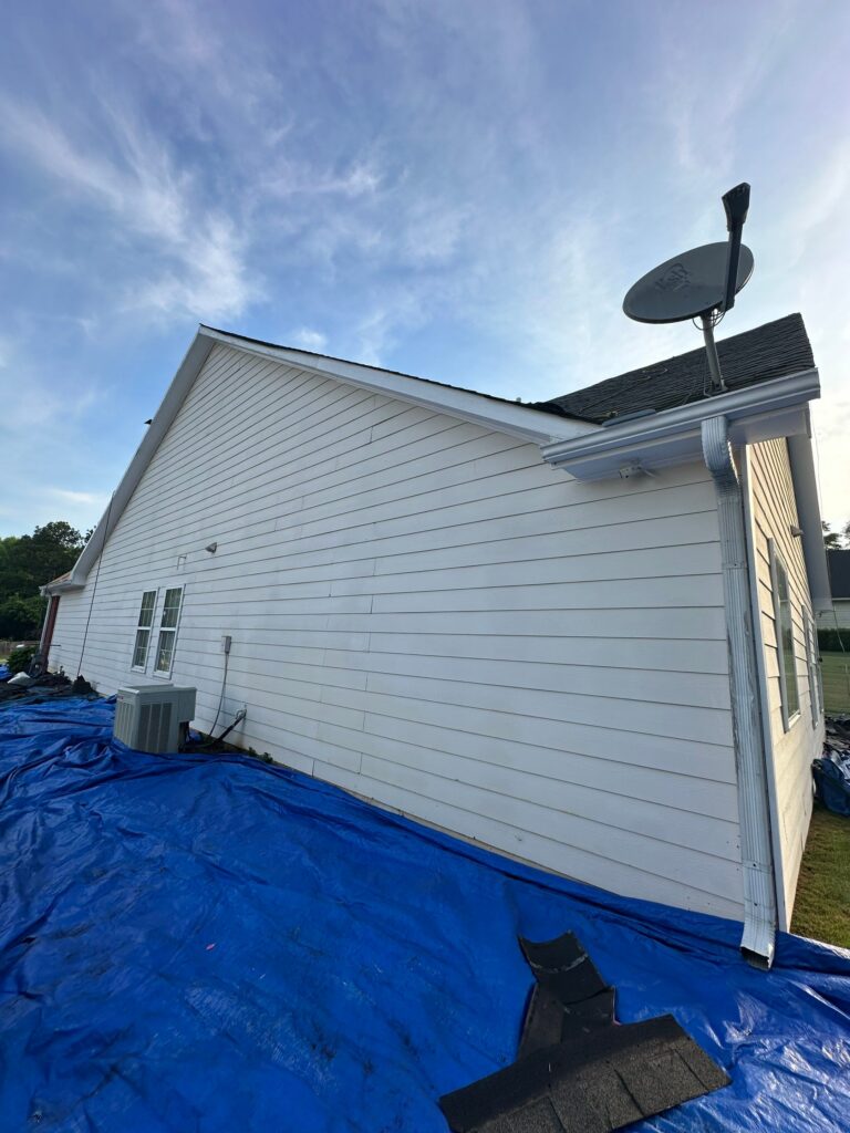 White residential home exterior with blue tarp covering the ground during roof maintenance